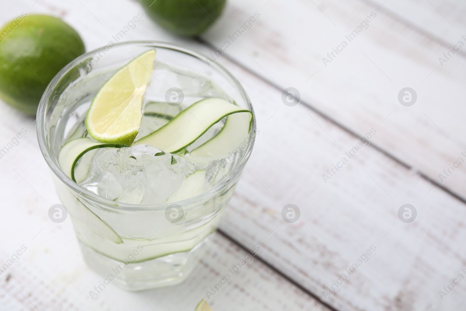 Photo of Refreshing water with sliced cucumber and lime in glass on white wooden table, closeup. Space for text