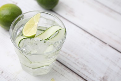 Refreshing water with sliced cucumber and lime in glass on white wooden table, closeup. Space for text