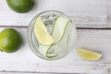 Refreshing water with sliced cucumber and lime in glass on white wooden table, top view