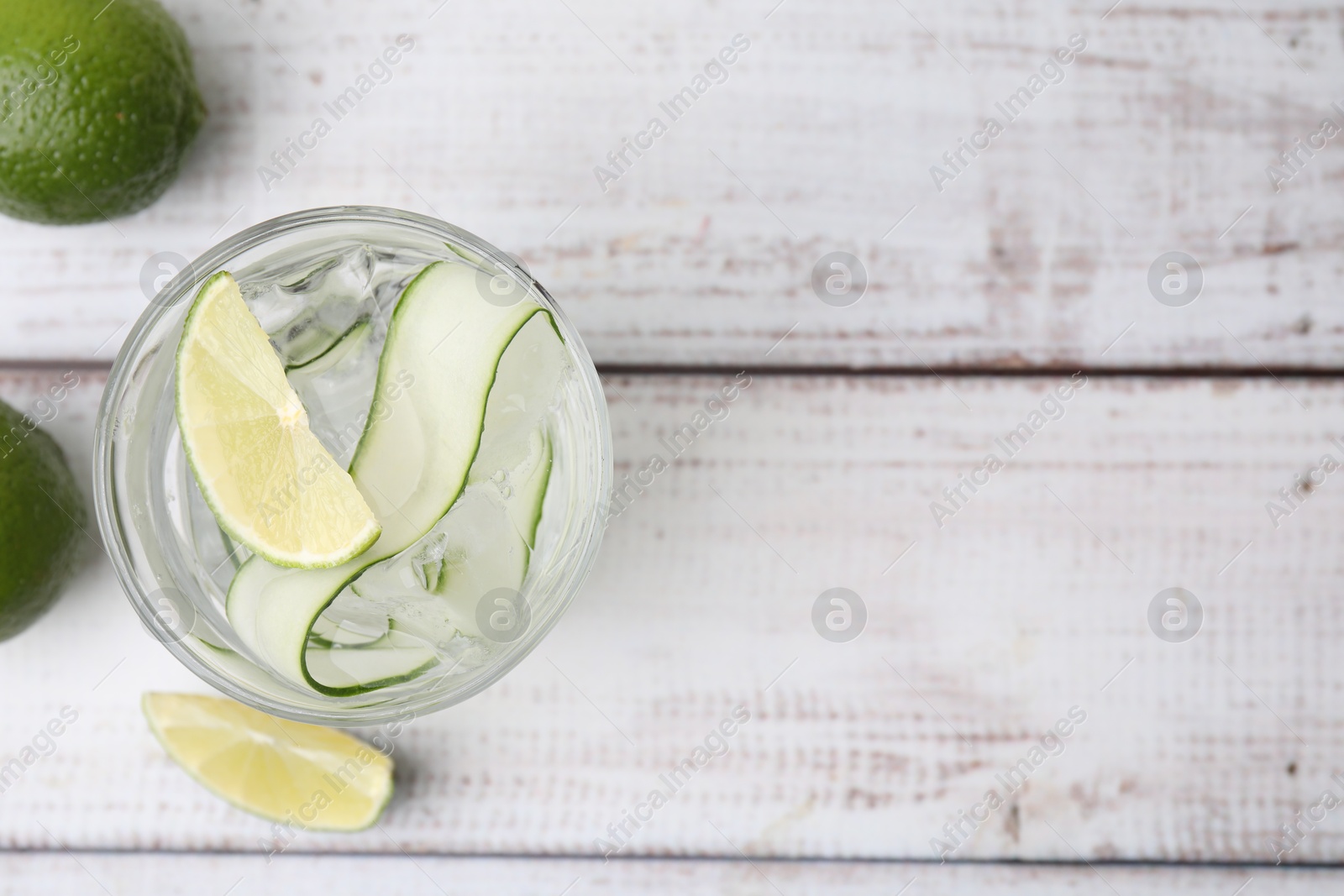 Photo of Refreshing water with sliced cucumber and lime in glass on white wooden table, top view. Space for text