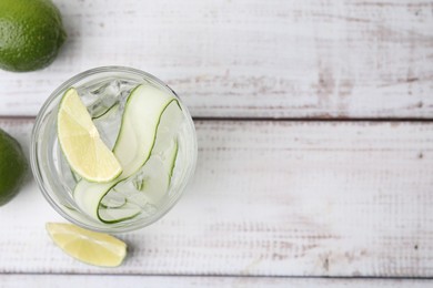 Photo of Refreshing water with sliced cucumber and lime in glass on white wooden table, top view. Space for text