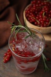 Photo of Refreshing water with red currants and rosemary in glass on wooden table, closeup