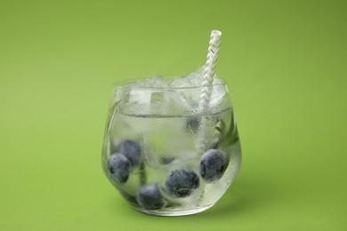 Refreshing water with blueberries and rosemary in glass on green background