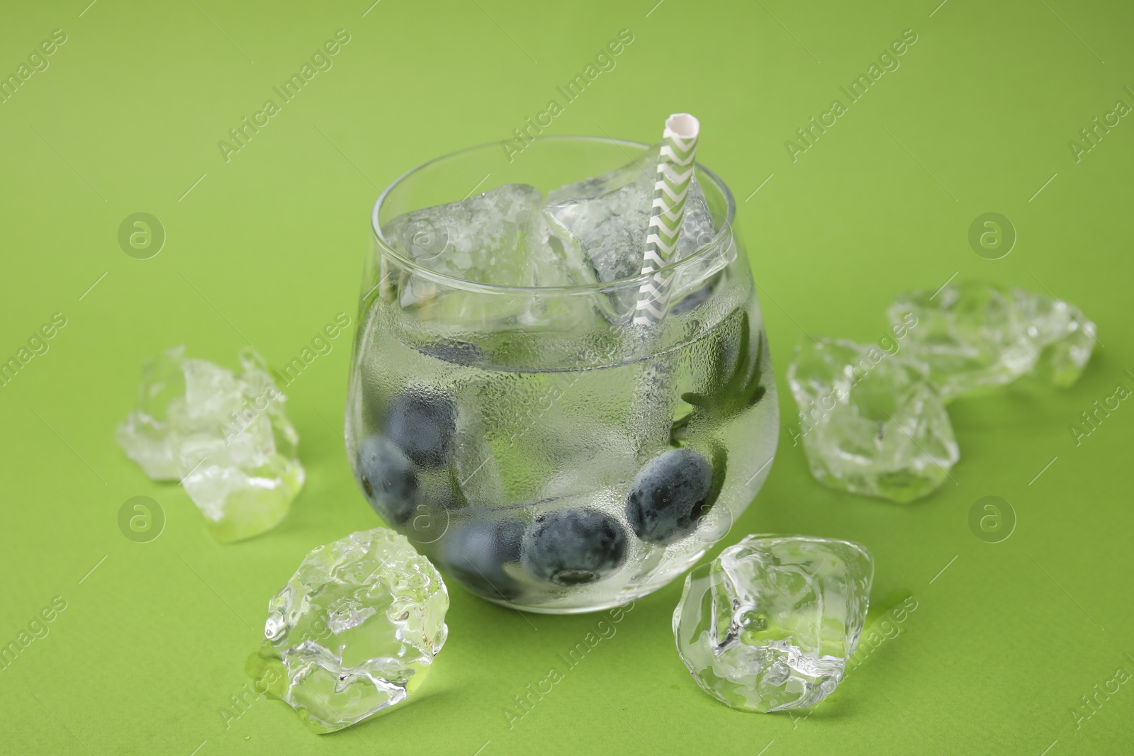 Photo of Refreshing water with blueberries, ice cubes and rosemary on green background