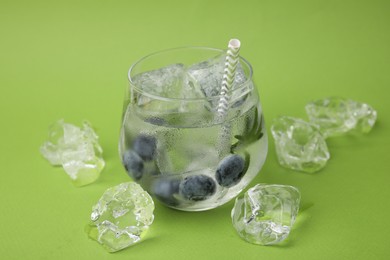 Photo of Refreshing water with blueberries, ice cubes and rosemary on green background