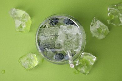 Refreshing water with blueberries and ice cubes on green background, top view