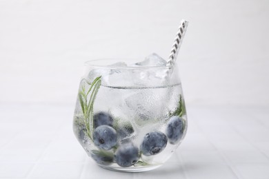 Photo of Refreshing water with blueberries and rosemary in glass on white tiled table