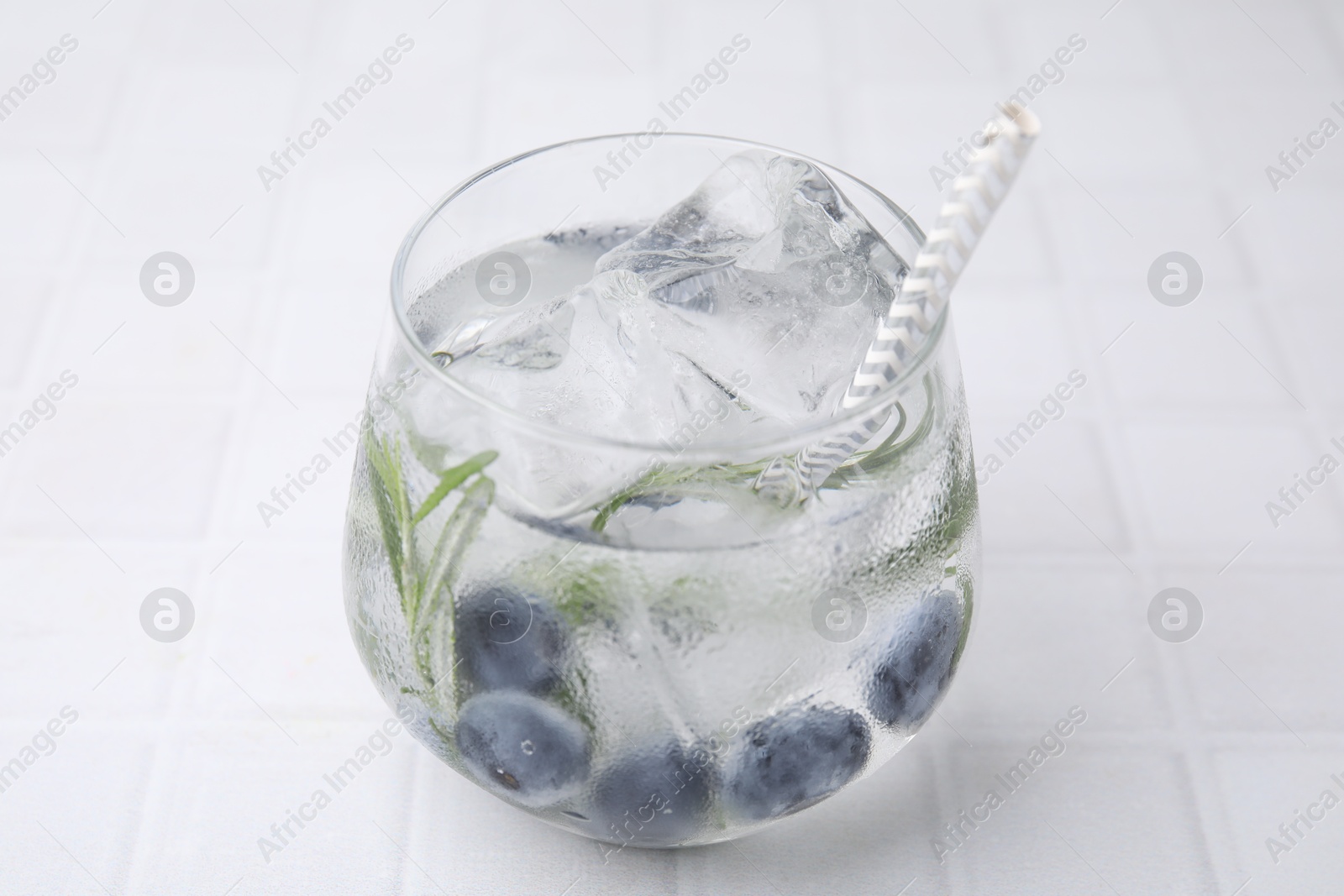 Photo of Refreshing water with blueberries and rosemary in glass on white tiled table