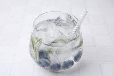 Photo of Refreshing water with blueberries and rosemary in glass on white tiled table