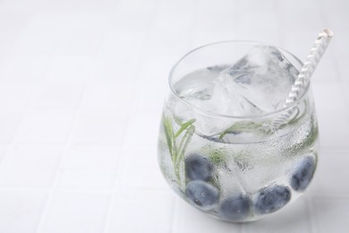 Photo of Refreshing water with blueberries and rosemary in glass on white tiled table, closeup. Space for text