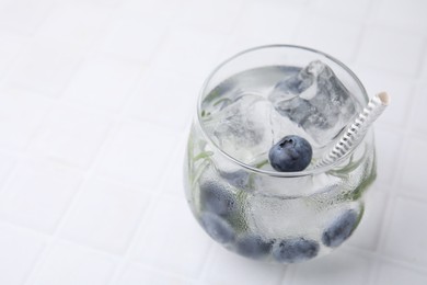 Photo of Refreshing water with blueberries and rosemary in glass on white tiled table, closeup. Space for text