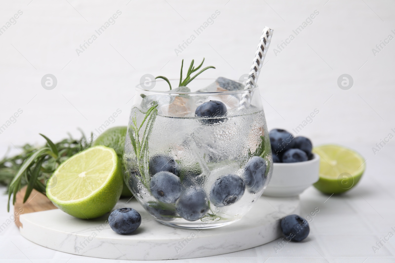 Photo of Refreshing water with blueberries and rosemary on white tiled table