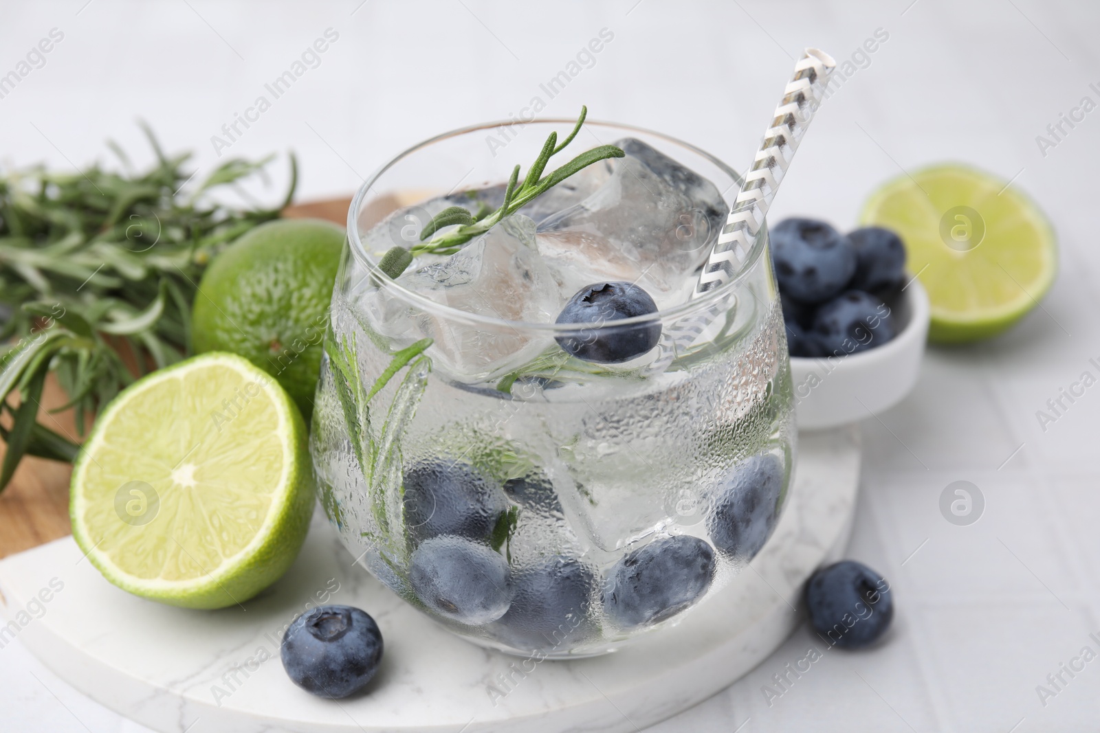 Photo of Refreshing water with blueberries and rosemary on white tiled table, closeup