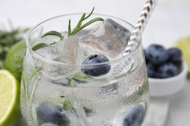 Refreshing water with blueberries and rosemary in glass on white table, closeup