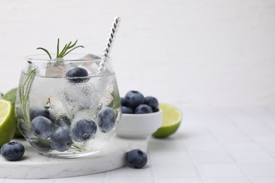 Photo of Refreshing water with blueberries and rosemary in glass on white tiled table, space for text