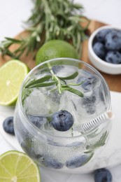 Photo of Refreshing water with blueberries and rosemary in glass on white table, closeup