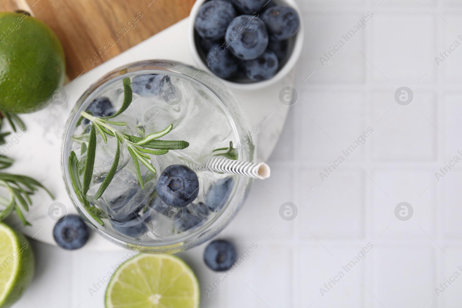 Photo of Refreshing water with blueberries and rosemary in glass on white tiled table, flat lay. Space for text