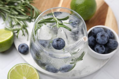 Photo of Refreshing water with blueberries and rosemary in glass on white table, closeup