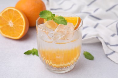 Photo of Refreshing water with orange and mint in glass on light table, closeup