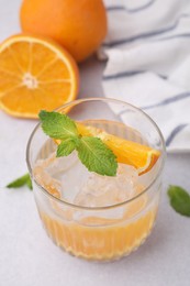 Photo of Refreshing water with orange and mint in glass on light table, closeup