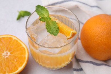 Refreshing water with orange and mint in glass on light table, closeup