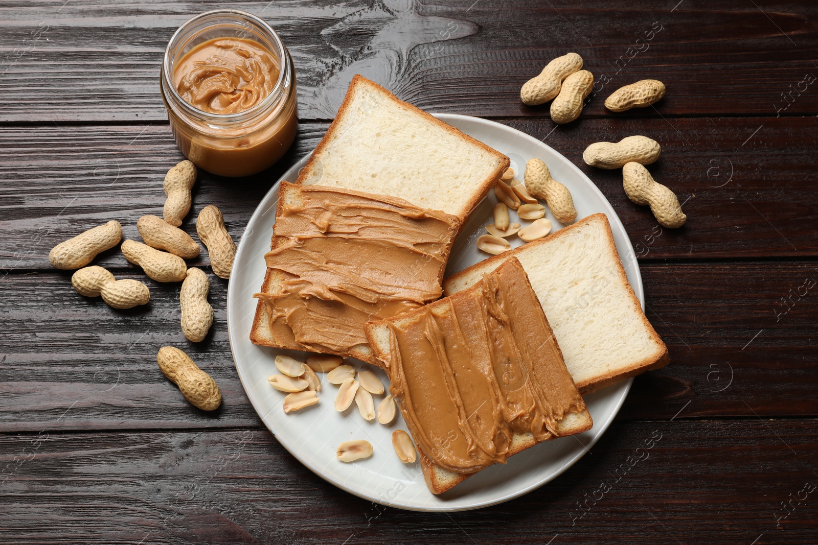 Photo of Delicious sandwiches with peanut butter and nuts on wooden table, flat lay