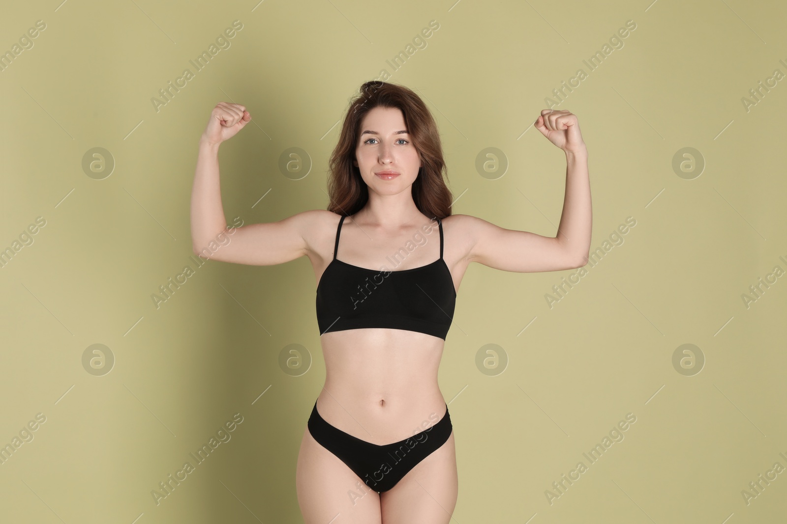 Photo of Woman with slim body showing muscles on olive background