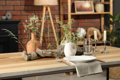 Set of clean dishware, vases with beautiful flowers, stones and burning candles on wooden table in stylish dining room