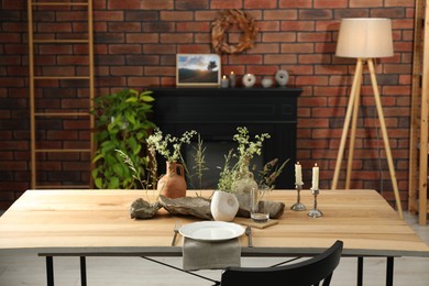 Set of clean dishware, vases with beautiful flowers, stones and burning candles on wooden table in stylish dining room