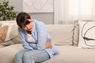 Photo of Upset woman suffering from abdominal pain on sofa at home