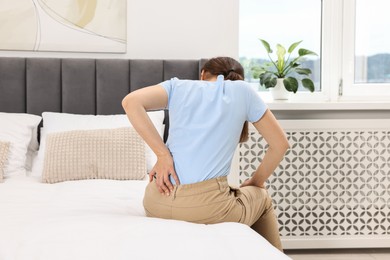 Photo of Woman suffering from back pain on bed at home, back view