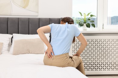 Woman suffering from back pain on bed at home, back view