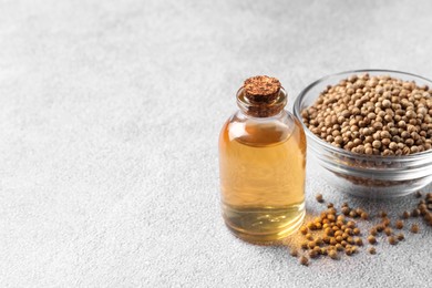 Photo of Coriander essential oil and seeds on grey table, space for text