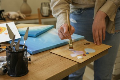 Photo of Woman with brush using palette at wooden table in drawing studio, closeup