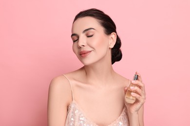 Beautiful woman with bottle of perfume on pink background