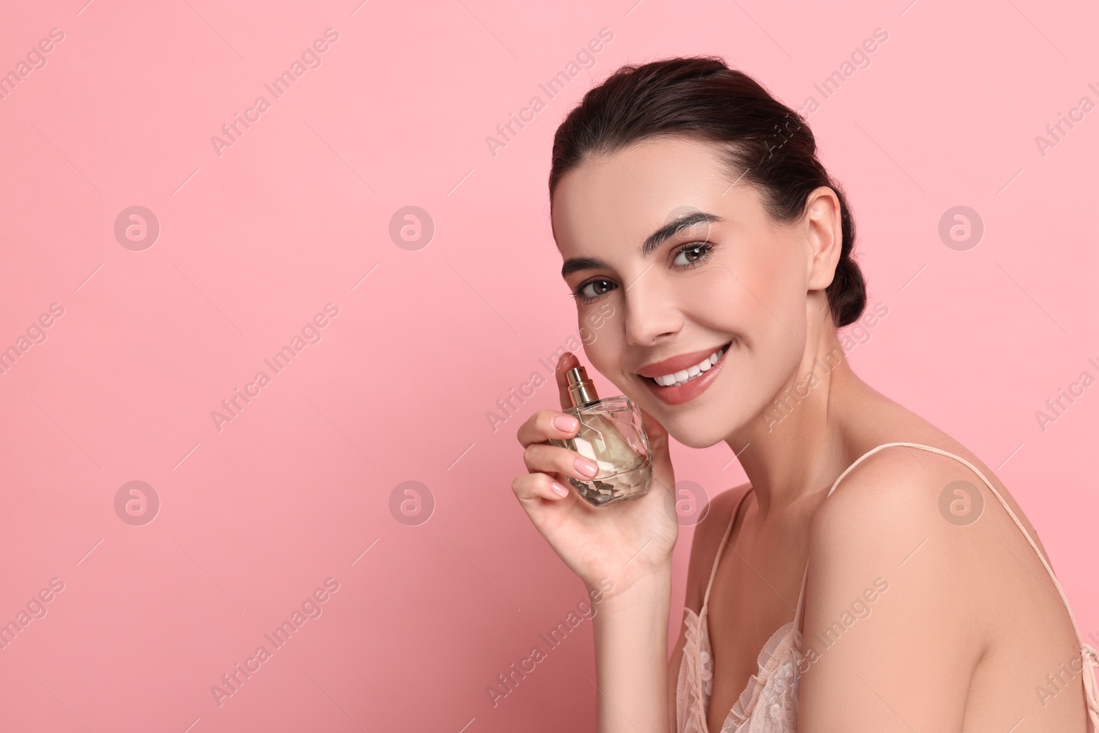 Photo of Smiling woman with bottle of perfume on pink background. Space for text