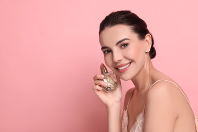 Photo of Smiling woman with bottle of perfume on pink background. Space for text