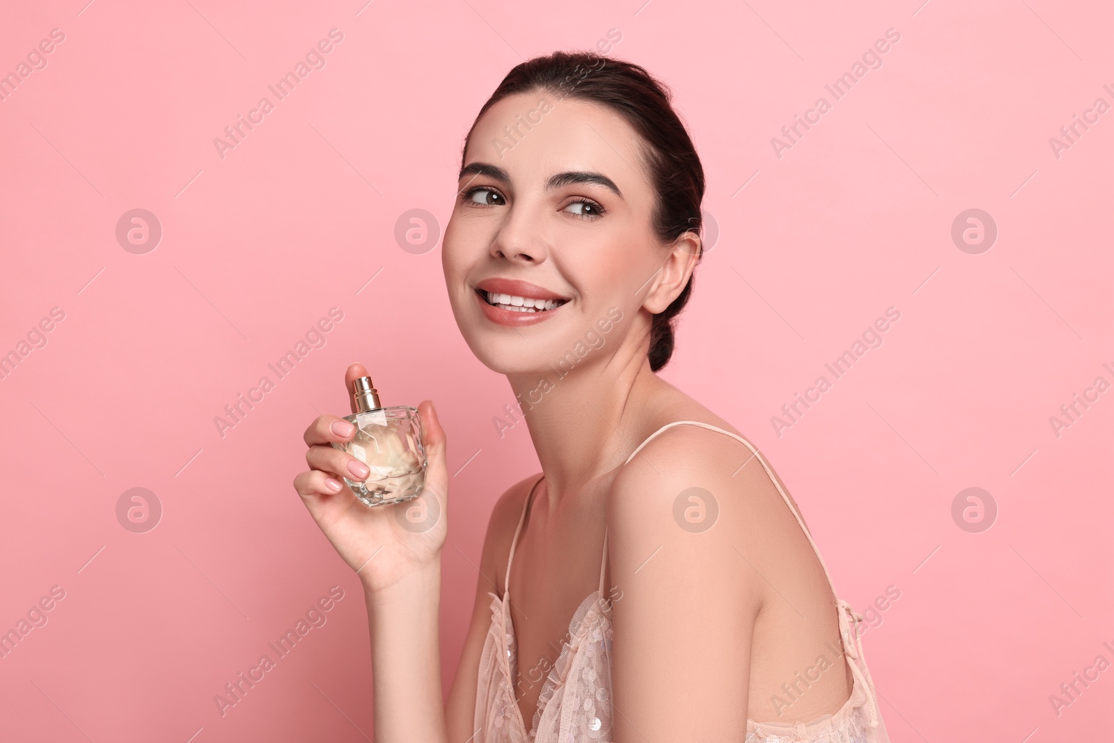 Photo of Smiling woman with bottle of perfume on pink background