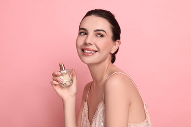 Smiling woman with bottle of perfume on pink background