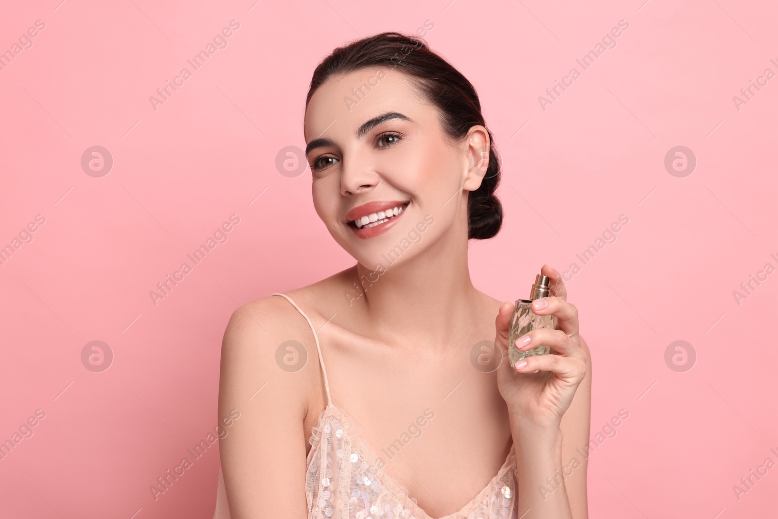 Photo of Smiling woman with bottle of perfume on pink background