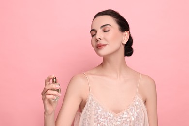 Beautiful woman spraying perfume on pink background