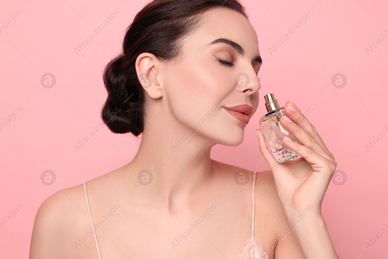 Photo of Beautiful woman smelling perfume on pink background