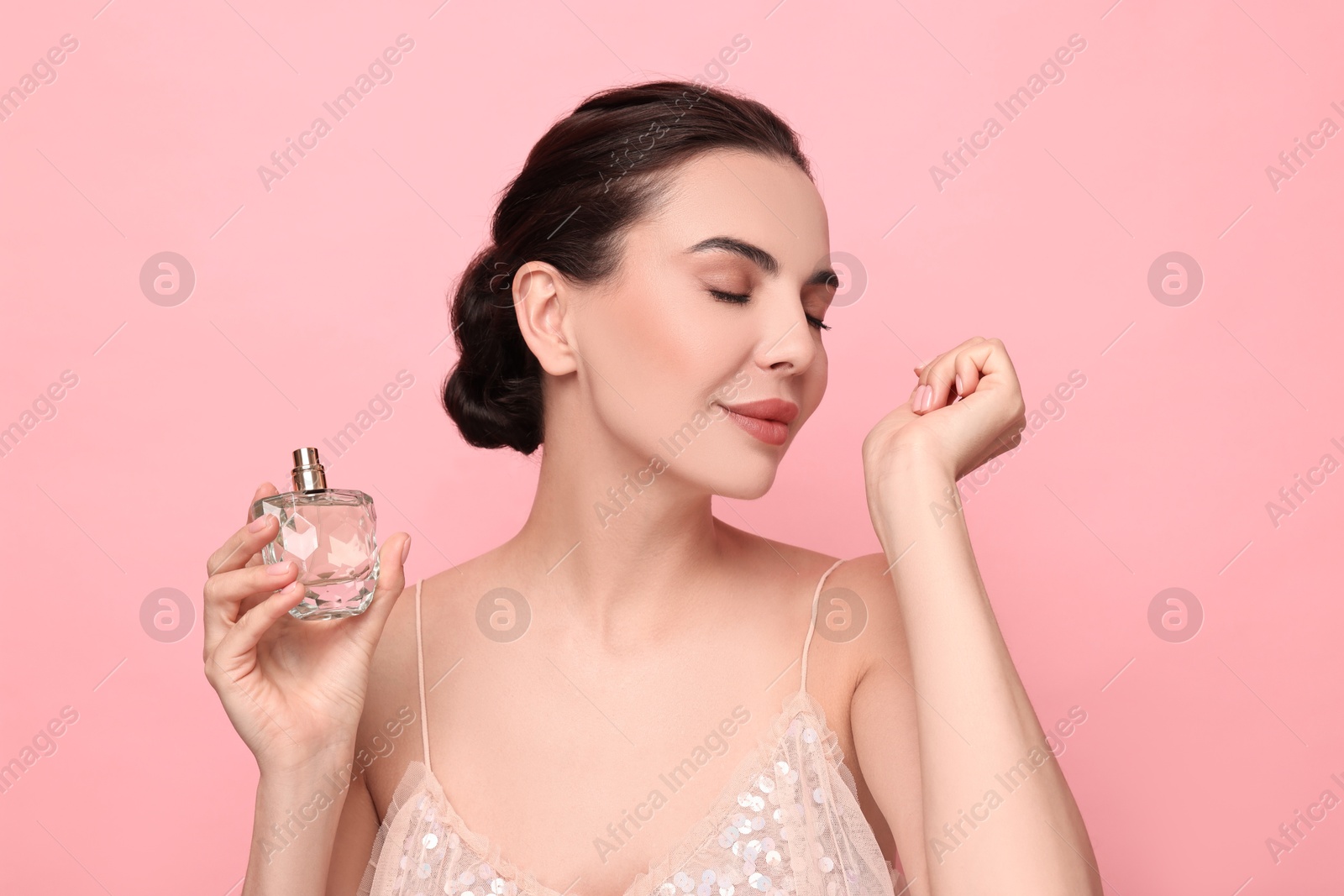 Photo of Beautiful woman smelling perfume on wrist against pink background