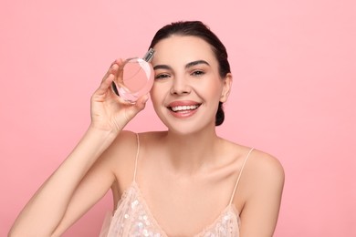 Photo of Smiling woman with bottle of perfume on pink background