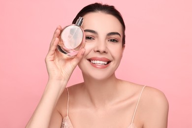 Photo of Smiling woman with bottle of perfume on pink background