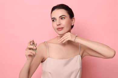 Beautiful woman with bottle of perfume on pink background