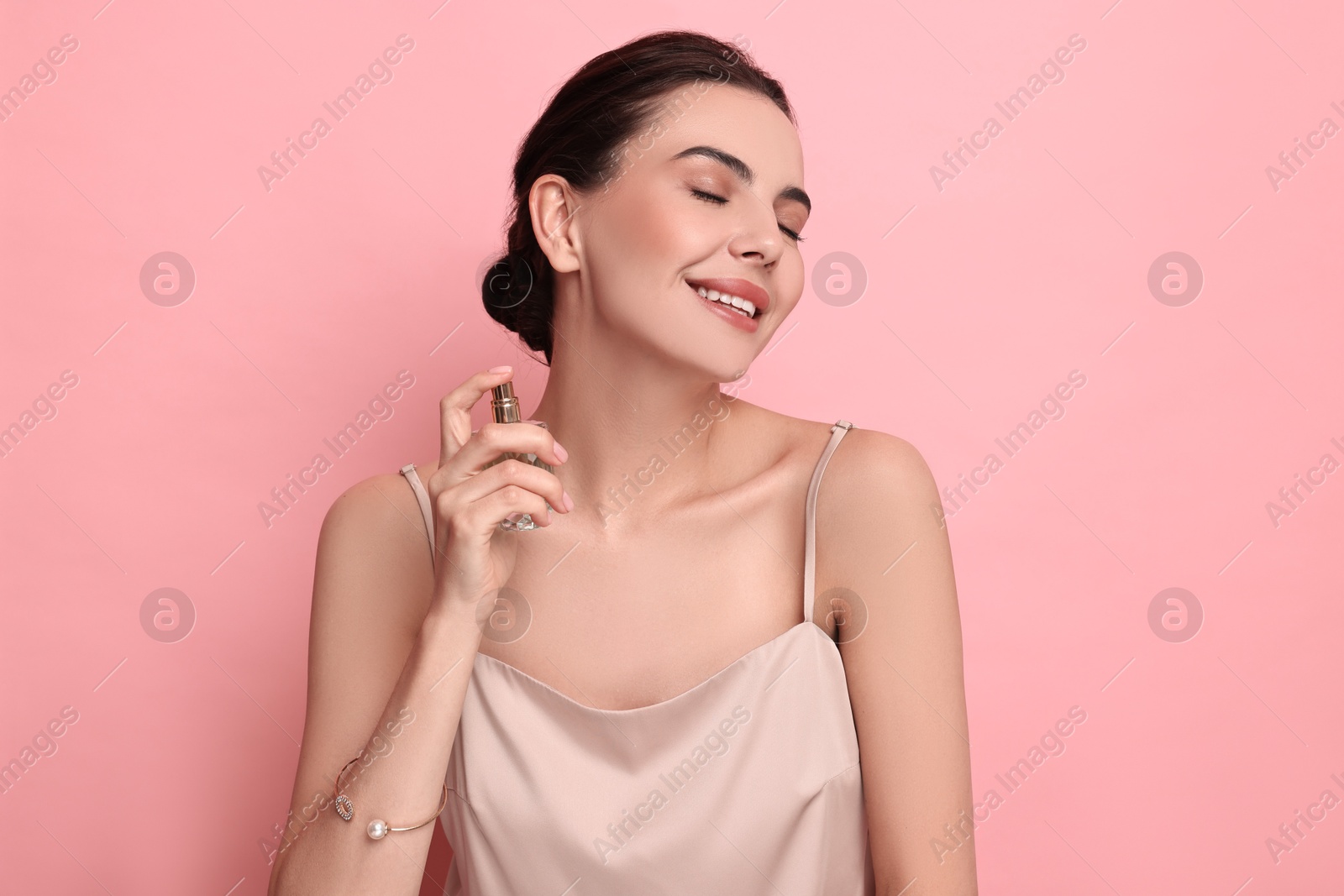 Photo of Smiling woman with bottle of perfume on pink background