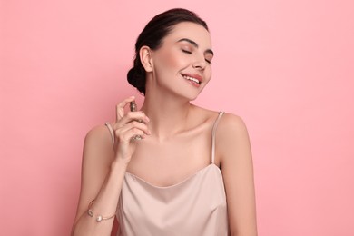 Photo of Smiling woman with bottle of perfume on pink background