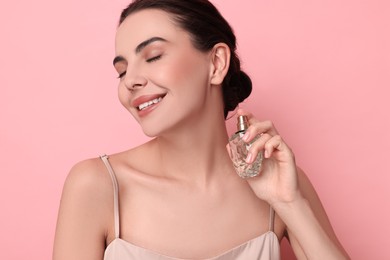 Smiling woman with bottle of perfume on pink background