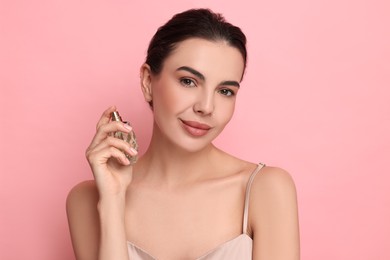 Beautiful woman with bottle of perfume on pink background